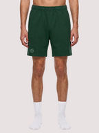 A model from the waist down wearing dark green athletic shorts with a small white circular logo on the left leg, paired with white socks, against a plain white background.